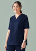 A woman models a navy scrub top featuring a V-neck and side pockets, with a logo on the sleeve. A woman models a navy scrub top featuring a V-neck and side pockets, with a logo on the sleeve.