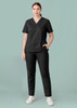 A woman is wearing a black scrub top with a V-neck and matching black pants, standing against a light green background.