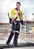 A man in a yellow and navy rugged cooling taped overall with a harness, standing on a construction site. A man in a yellow and navy rugged cooling taped overall with a harness, standing on a construction site.