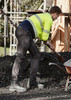 A man in high-visibility workwear and black stretch pants shovels gravel at a construction site. A man in high-visibility workwear and black stretch pants shovels gravel at a construction site.