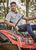 A man wearing a grey short sleeve button-up shirt sits on a red Kubota lawn mower amidst greenery. A man wearing a grey short sleeve button-up shirt sits on a red Kubota lawn mower amidst greenery.