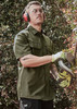 A man wearing an olive green short sleeve button-up shirt, safety glasses, and ear protection, using a power tool.
