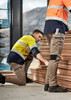 Two workers in high-visibility jackets and stretch cuffed pants, stacked wood planks in an industrial setting. Two workers in high-visibility jackets and stretch cuffed pants, stacked wood planks in an industrial setting.