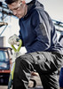 A man in a navy blue unisex multi-pocket hoodie, wearing gloves, kneels with a spade in a work environment.