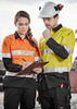 Two workers in high-visibility long sleeve shirts, one orange and one yellow, discussing a clipboard while wearing protective gear.
