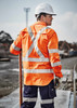 Hi-vis orange long sleeve shirt with reflective tape, worn by a worker on a construction site, featuring a helmet and gloves.