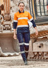 A woman in an orange and navy work outfit with reflective stripes stands near heavy machinery. The outfit includes cargo pants. A woman in an orange and navy work outfit with reflective stripes stands near heavy machinery. The outfit includes cargo pants.