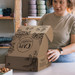 A woman is assembling a brown die cut box with a locking lid, featuring coffee bean illustrations and a logo.