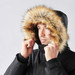 A black parka jacket featuring a fur-lined hood, worn by a man adjusting the hood around his face.