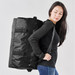 A medium black duffle bag featured being carried by a person, with adjustable straps and buckles visible.