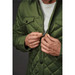 A green quilted jacket with a zip and button closures, featuring chest pockets and a close-up of hands zipping it up. A green quilted jacket with a zip and button closures, featuring chest pockets and a close-up of hands zipping it up.