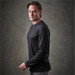A man wearing a black long sleeve t-shirt, posing against a textured background. The shirt features branding.