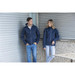 A navy unisex shell jacket with a hood is worn by both a male and female model, featuring a logo. A navy unisex shell jacket with a hood is worn by both a male and female model, featuring a logo.