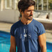 A navy blue crew neck T-shirt featuring a logo on the front. The model is outdoors by a pool.