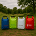Four dry bags in blue, green, white, and red, featuring logos on each bag, set in a grassy outdoor area.