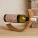 A wine bottle rests in a curved, wooden holder, showcasing a blend of natural wood tones and a pink label.