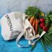 A cotton shopping tote in cream with a mesh top, filled with carrots, radishes, and fresh herbs. A cotton shopping tote in cream with a mesh top, filled with carrots, radishes, and fresh herbs.