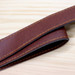 A brown leather strap with yellow stitching, laid on a wooden surface. The strap has a smooth finish and a sturdy appearance.