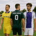 Three players in sports jerseys: a yellow jersey with blue trim, a green goalkeeper kit, and a white jersey with purple accents.