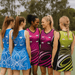A group of women wearing colourful A-line netball dresses featuring various designs in blue, pink, and black.