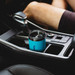 A drink bottle in a car cup holder, featuring a turquoise body and a black lid. It has a logo on the side.