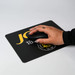 A black fabric mouse mat with a hand using a black mouse, featuring a logo and yellow text. A black fabric mouse mat with a hand using a black mouse, featuring a logo and yellow text.