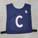 A navy blue pull-over elastic netball bib with a large white ‘C’ and a branding logo.