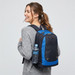 A backpack in black and blue, featuring a drink bottle in a side pocket, worn by a smiling person.