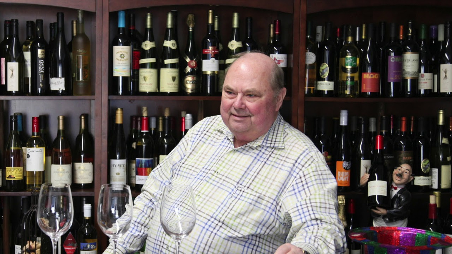 Bruce Neyers seated before a wall of wine bottles