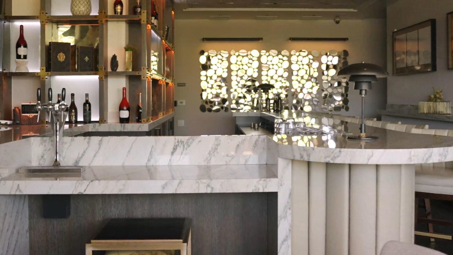 A marble tasting-room bar with a tap tower, backlit bottle cubbies, and a pebble-glass window.