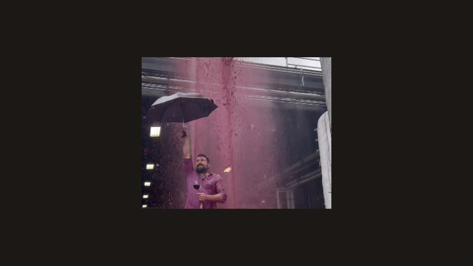 A man holding an umbrella under a fall of red wine.