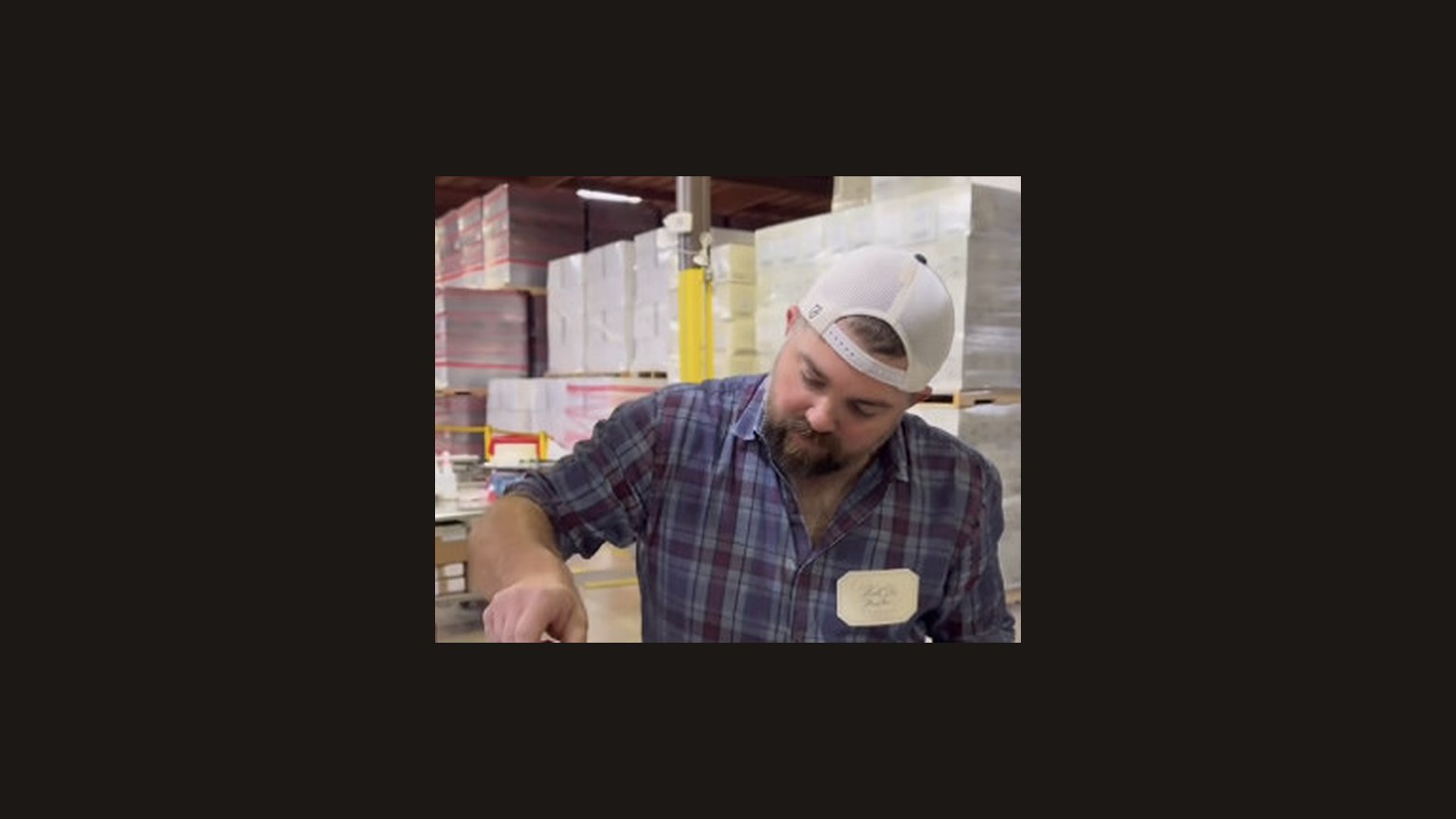 A man in a plaid shirt dipping a bottle in red wax.