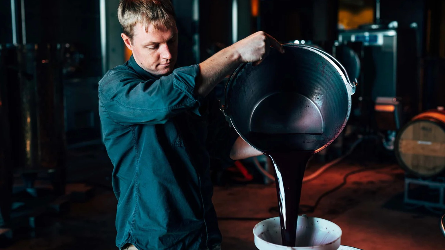 Austin Peterson pouring dark wine from a bucket through a funnel