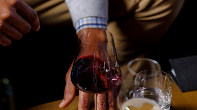 A hand around a glass of red wine on a wood table at the winery