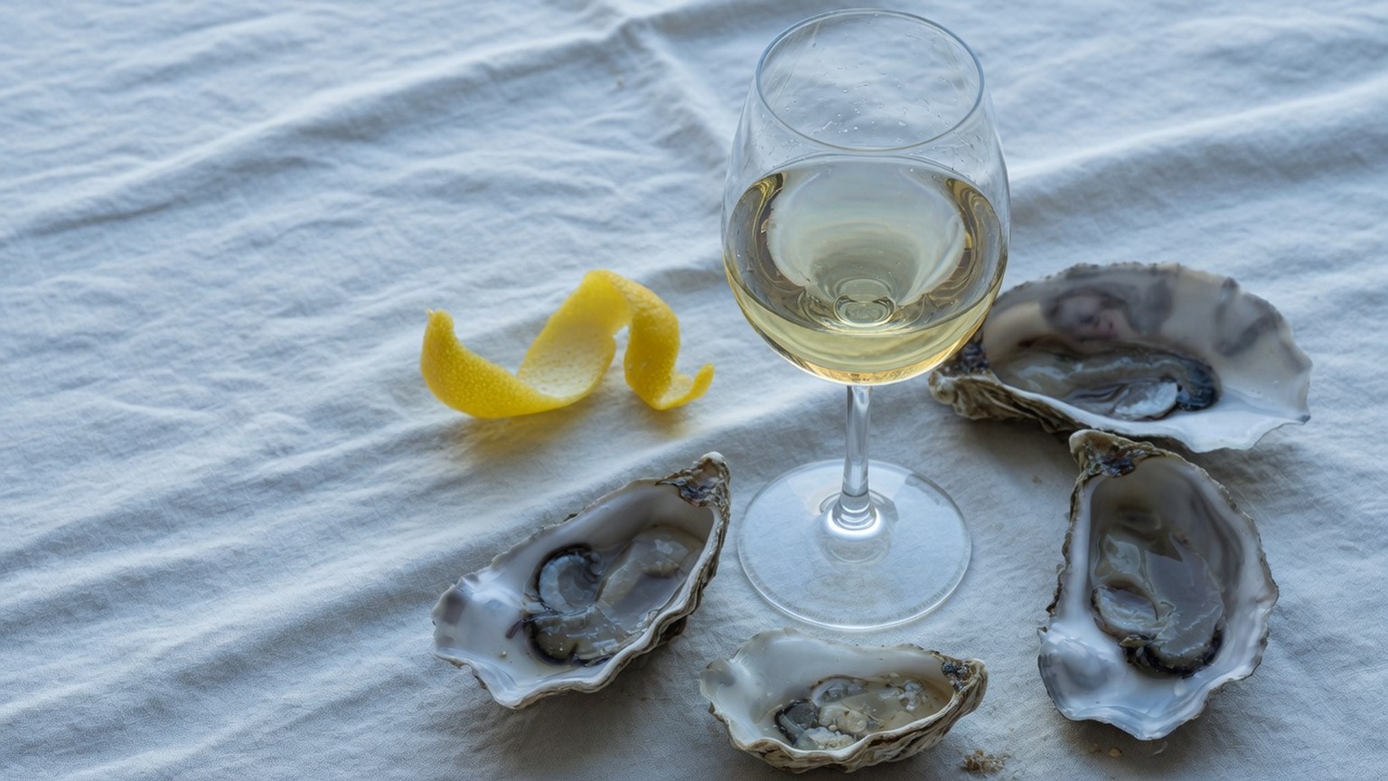 A glass of pale white wine with oyster shells and lemon peel