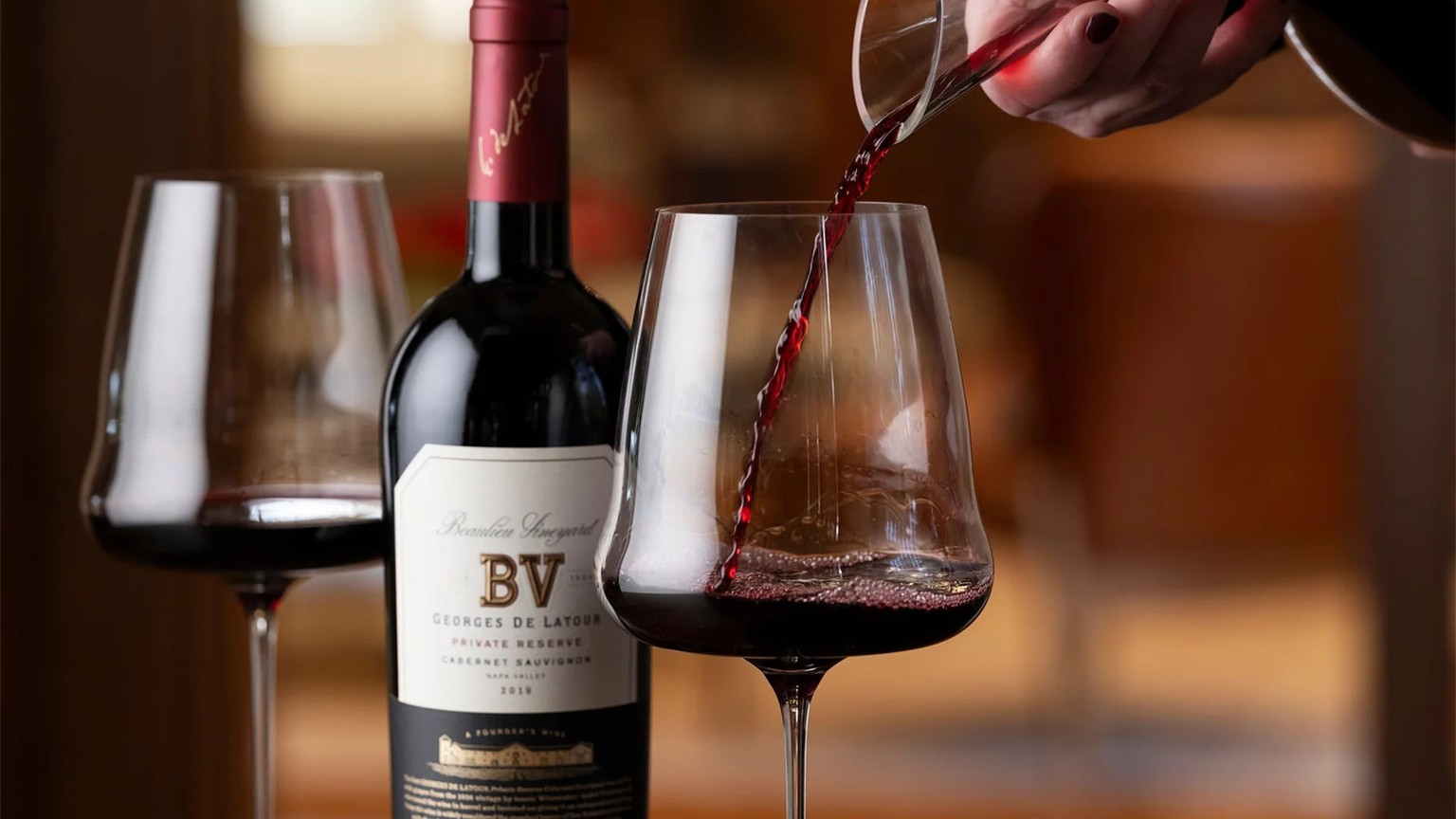 Red wine poured from a decanter into a glass, with a 2019 Georges de Latour bottle behind it