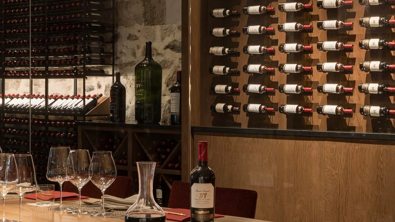 A long oak table set with a Georges de Latour bottle, a decanter, and a wall of wines