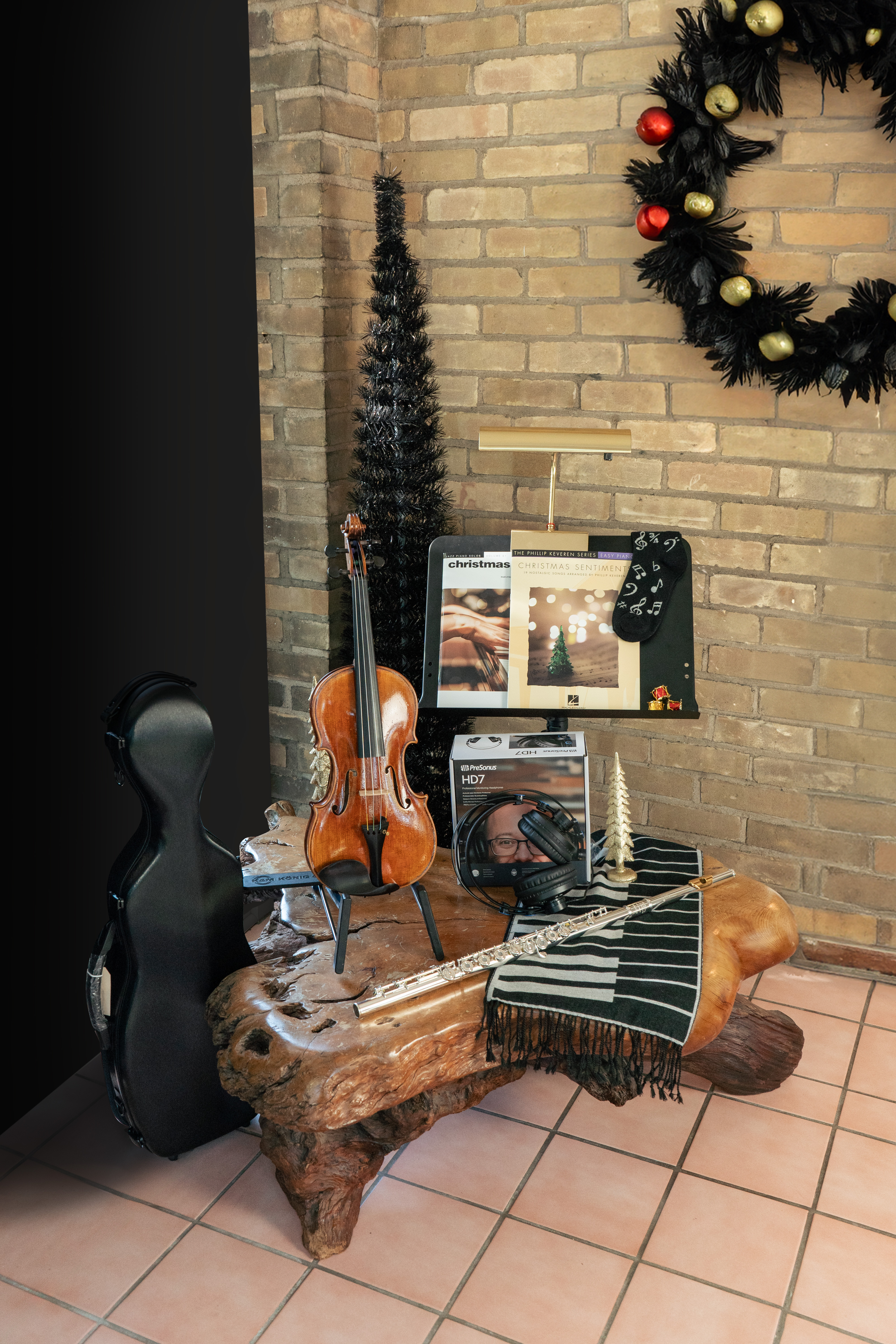A Gianna Rose violin with case and accessories is displayed next to a Haynes Bravo flute, all in front of a brick wall decorated for Christmastime.