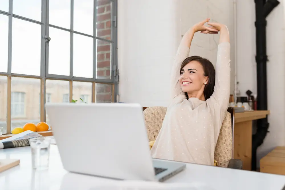 An employee stretching at her desk beside a laptop