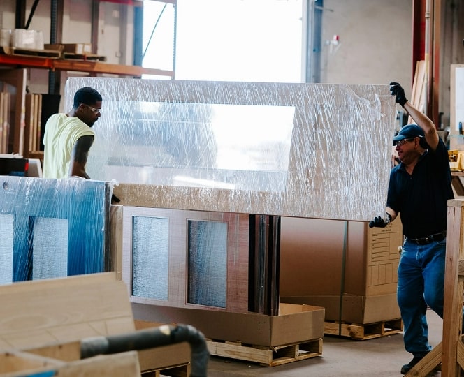 Workers handling large packaged wood doors inside a manufacturing warehouse