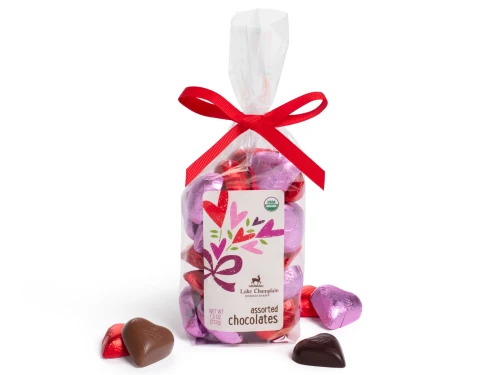 Organic milk and dark chocolate Valentine hearts wrapped in pink and red foils and packaged n a clear gift bag with a dark pink bow at the top.