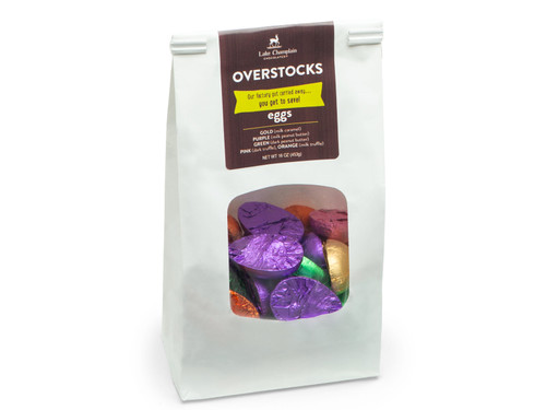 White paper bag with a clear window showing chocolate eggs wrapped in assorted colorful foils and a brown label that says "overstock eggs" on it.