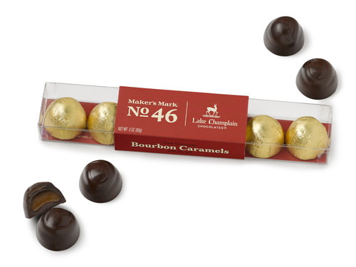 Dark chocolate Maker's Mark® 46 Bourbon caramels wrapped in gold foil and packaged in a clear gift box with a dark red sleeve and unwrapped caramels around the gift box.