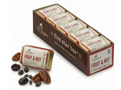 Ten dark chocolate fruit and nut five star bars sitting in a long rectangular box with a fruit and nut five star bar sitting on the left of the box with pieces of chocolate, dried fruit and pecans around the bar.