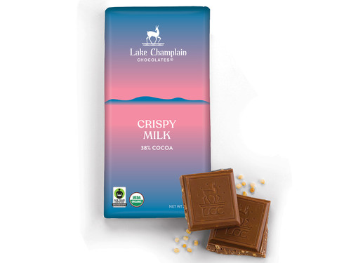 Milk chocolate crunchy quinoa bar in a light blue and pink wrapper with two square pieces of chocolate in front of the bar with little pieces of quinoa next to them.