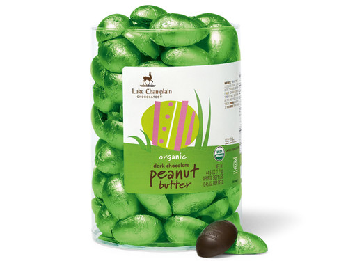 Organic dark chocolate peanut butter filled eggs wrapped in green foil and packaged in a clear plastic dispenser with an unwrapped egg and a wrapped egg sitting in front of the dispenser.
