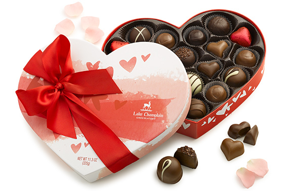 Assorted gourmet chocolates in a heart shaped gift box for Valentine's Day with a red bow around the box.