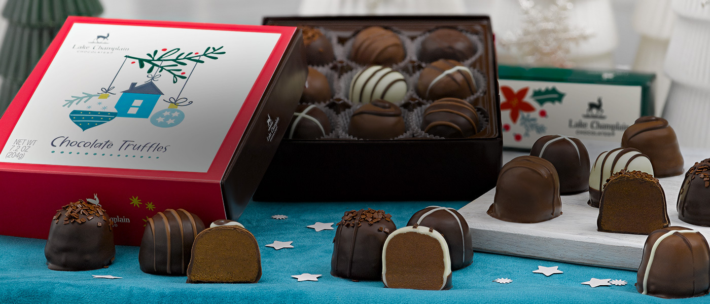 Assorted Christmas chocolates in Christmas themed gift boxes with milk chocolate Santa and a dark chocolate snowman under a Christmas tree with teal-blue and cream decorations on it and teal and white packages under it.