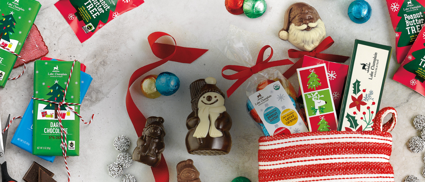 Assorted Christmas chocolates sticking out of a red and white stripped stocking with holiday chocolate bars , chocolate snowmen and bon bons around the stocking.