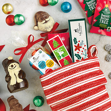 Assorted holiday chocolates in a red and white stripped stocking with wrapped and unwrapped Christmas themed chocolates around the stocking.